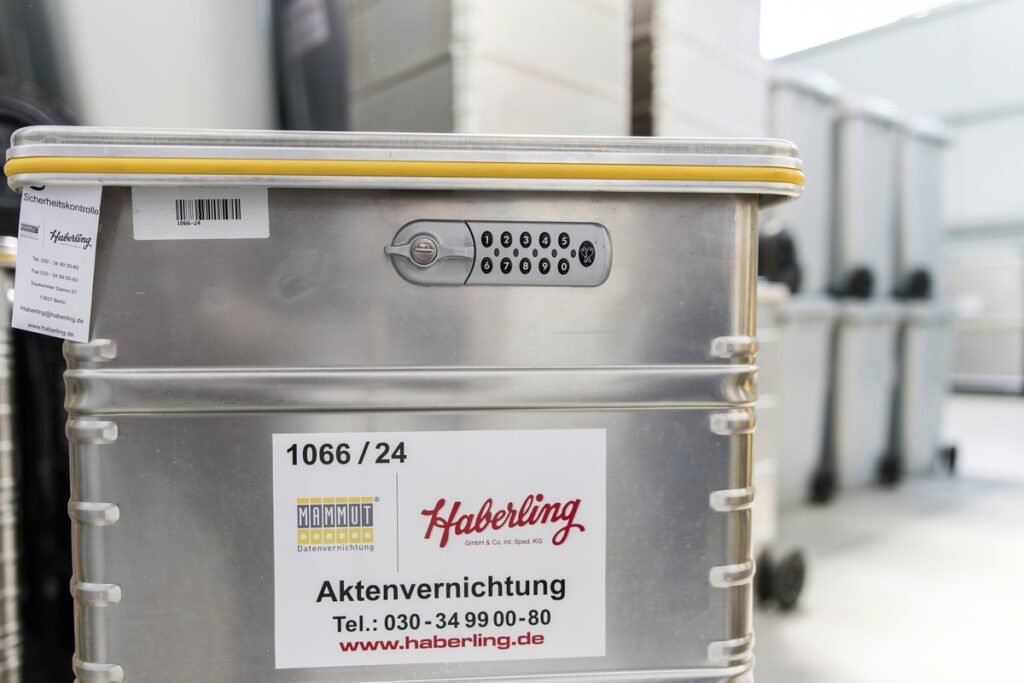 Im Fokus steht ein Metallbehälter mit einem Zahlenschloss, der mit „Haberling“ beschriftet ist. Im Hintergrund ist eine Reihe ähnlicher Behälter verschwommen zu sehen.