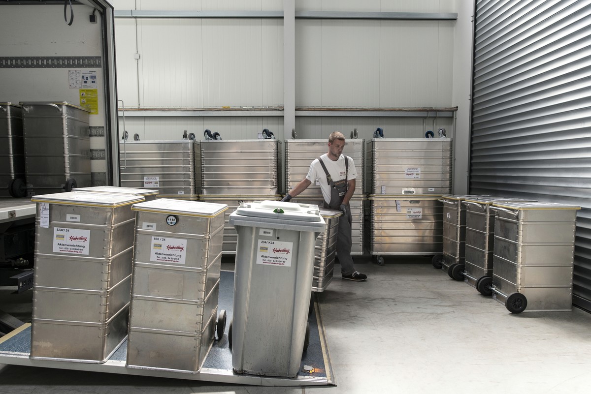Mitarbeiter in Arbeitskleidung lehnt an gestapelten Metallcontainern in einem Lagerhaus.