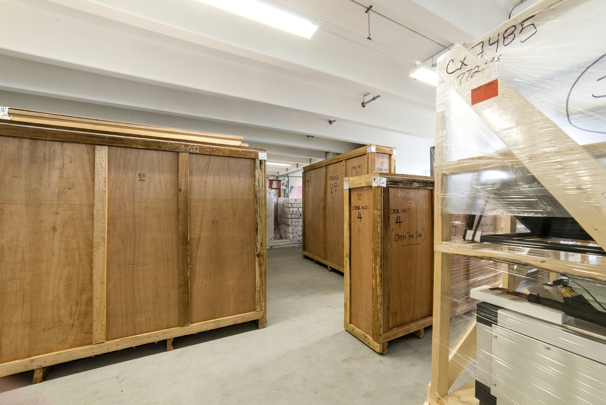 Ein Lagerbereich mit großen Holzkisten, umgeben von verpackten Gegenständen auf Paletten. Der Raum ist hell, übersichtlich und industriell gestaltet.