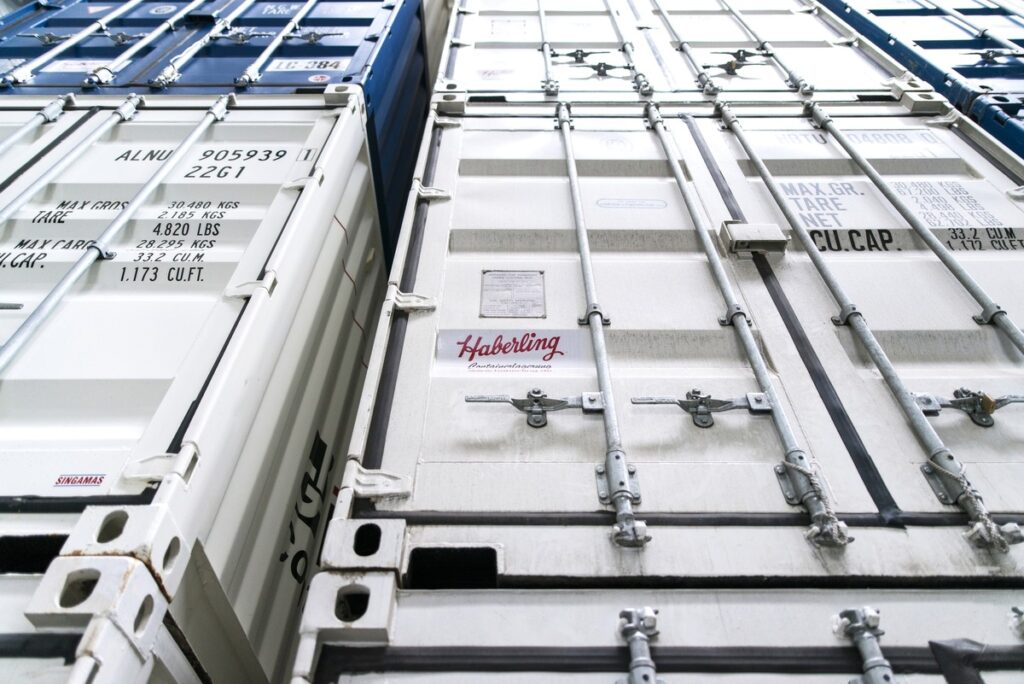 Nahaufnahme von gestapelten Versandcontainern in Blau und Grau mit Metallschlössern und aufgedrucktem Text.