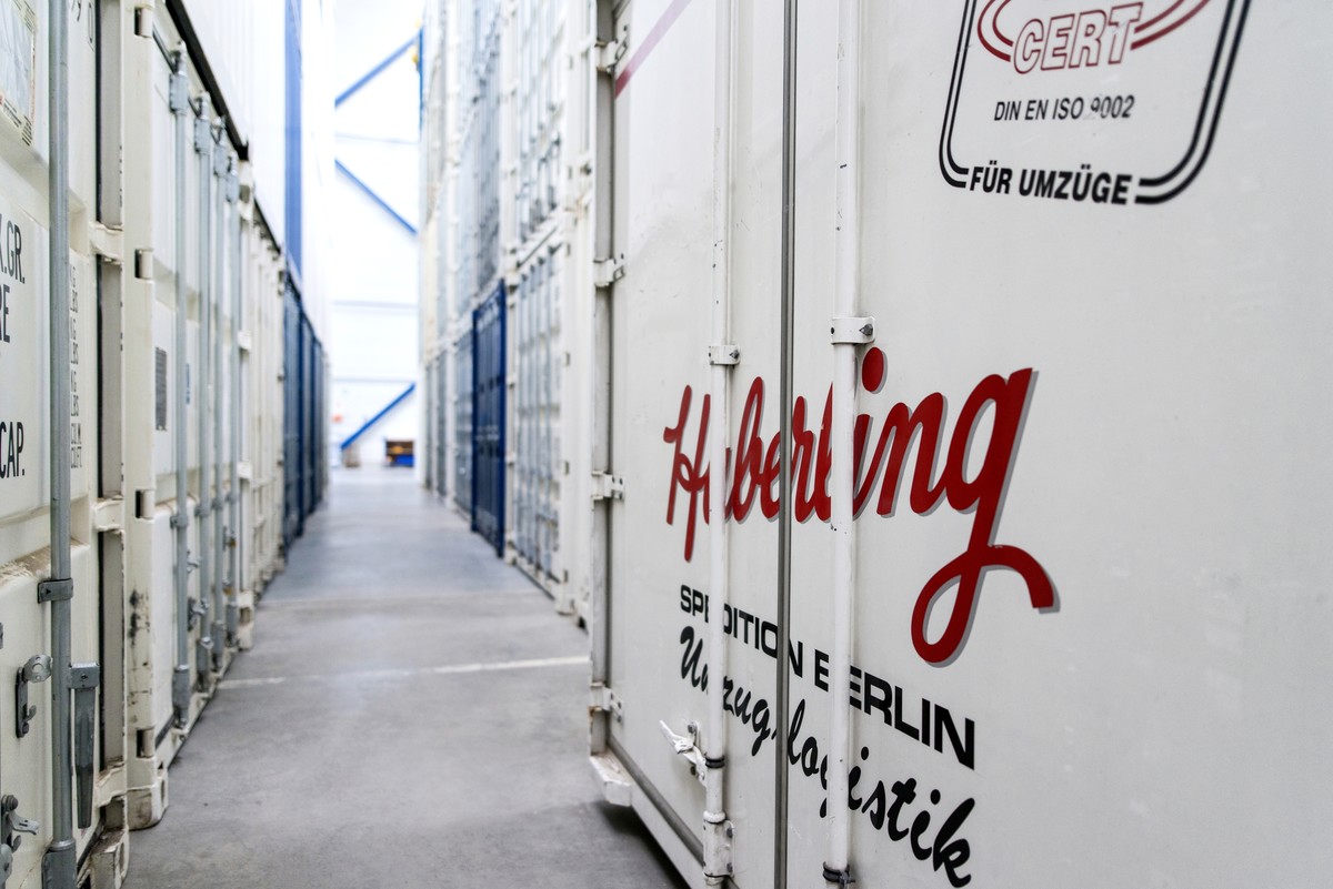 Schmaler Gang zwischen hohen weißen Lagercontainern in einem Lagerhaus. Roter Text "Haberling" auf dem nächstgelegenen Container.